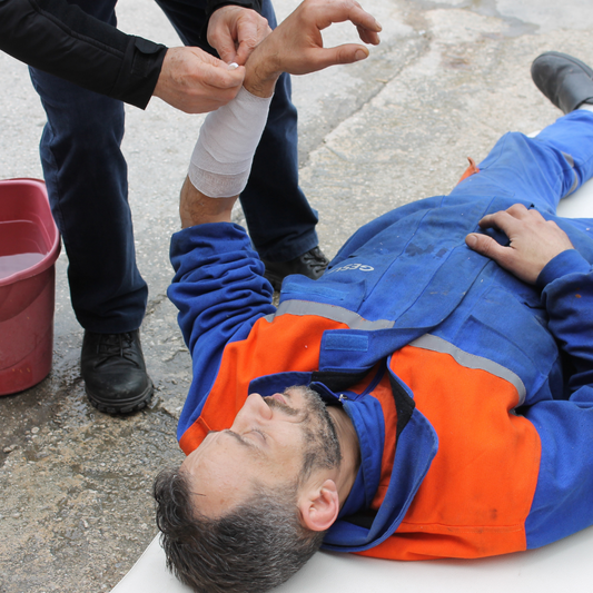 A person carefully wrapping a bandage around a man's arm. The scene depicts first aid being administered, with a focus on providing care and assistance. This image reflects a moment of medical attention and support for someone in need