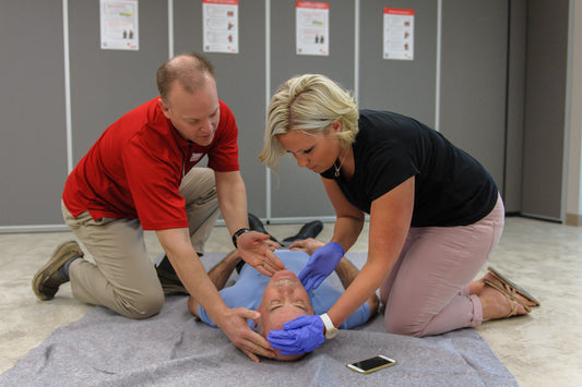 A first aid instructor, demonstrating the technique of opening the airway to a student. The instructor is shown tilting the head of the student backward, illustrating proper technique for maintaining an open airway. This image captures a teaching moment in a first aid training session, emphasizing fundamental lifesaving skills.